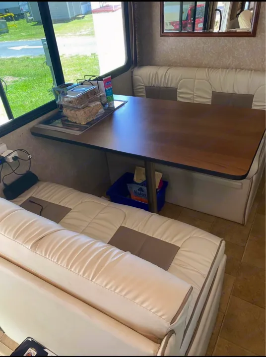 Inside an RV rental: a bright dinette with cream and gray benches, a wood table, and views of the outdoors.. Hurricane F53 2010