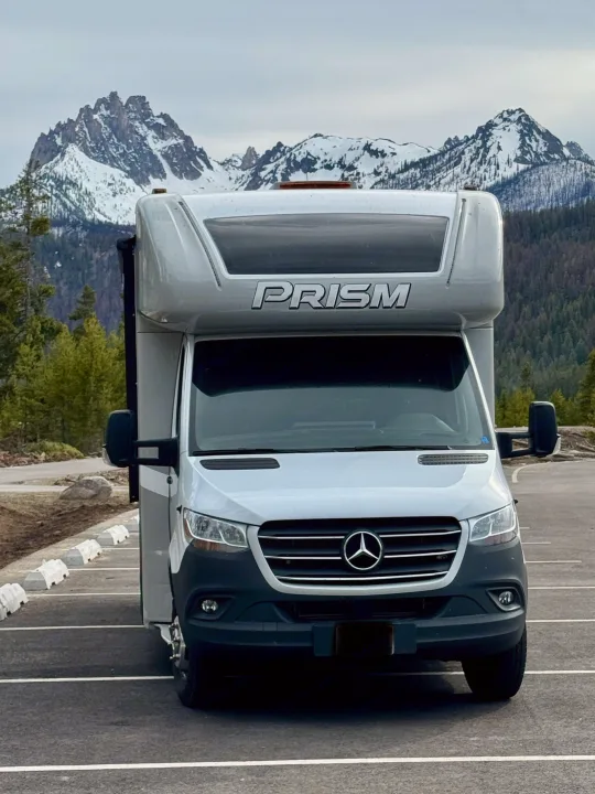 Grey Mercedes-Benz Prism RV rental parked, with majestic snow-capped mountains in the background, ideal for travel.. Coachman Prism Select 24 CB 2021