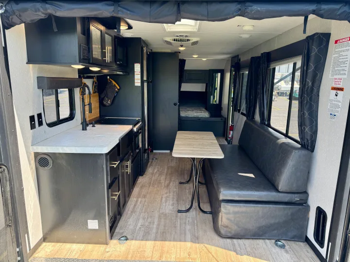 Spacious RV rental interior: kitchen with sink/stove, dining area with table/bench, and bed, offering a comfortable living space.. Forest River Grey Wolf 2021