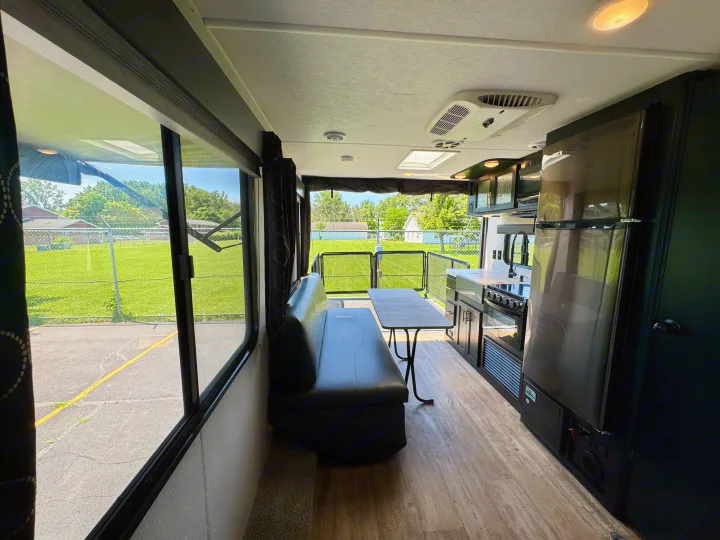 Step inside this RV rental: A well-lit living area features a black bench, table, and full kitchen, with outdoor green views.. Forest River Grey Wolf 2021
