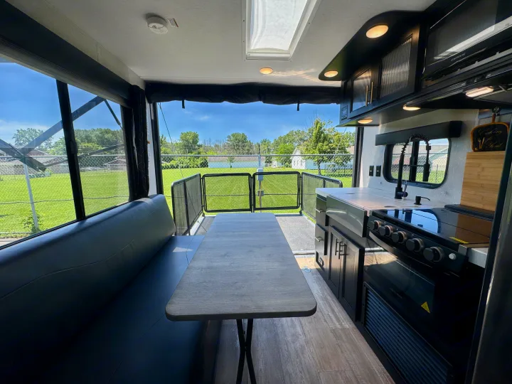 Inside a modern rv rental: dining booth, full kitchen with stove, and open ramp to scenic outdoor views.. Forest River Grey Wolf 2021