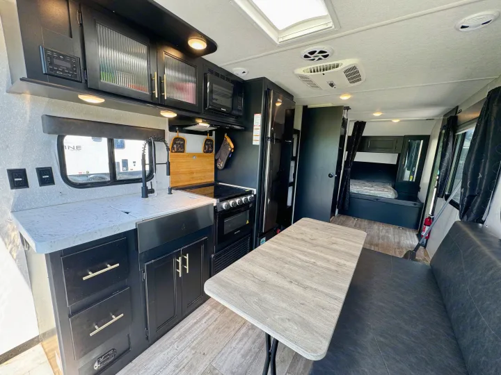 Modern rv rental interior: kitchen, dining, & bedroom. Features black cabinets, light counters, wood-look floor, skylight & AC.. Forest River Grey Wolf 2021
