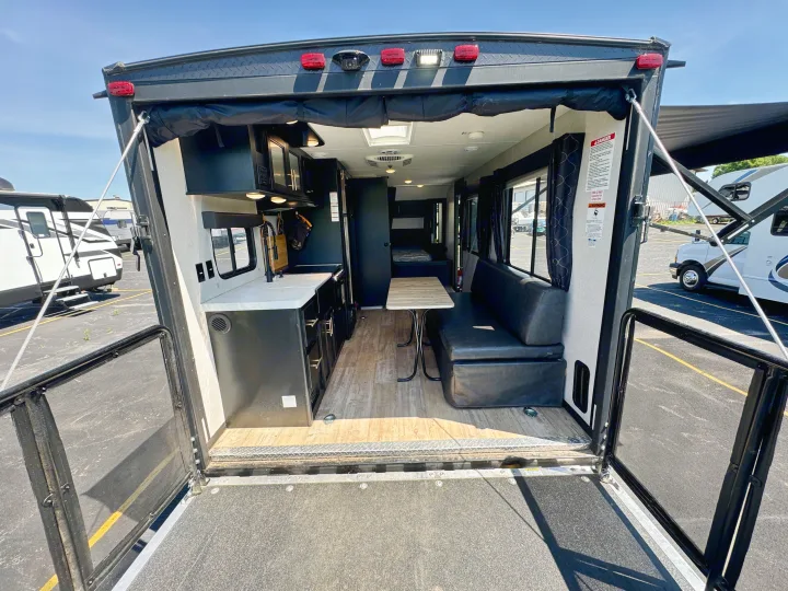 Step inside this RV rental toy hauler with its ramp door open, showcasing a modern interior, kitchen, and living area.. Forest River Grey Wolf 2021