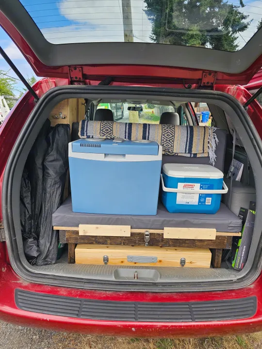 Minivan's rear converted for camping: platform bed, coolers, blanket. An affordable RV rental alternative.. Dodge Caravan 2006