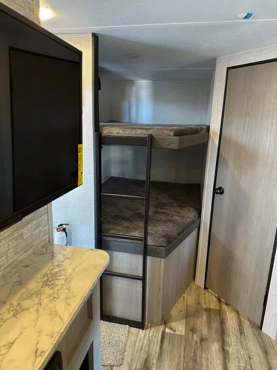 Cozy RV rental featuring bunk beds with ladder, TV, and modern counter. Ideal for group stays.. Coleman Dutchman Light 2023