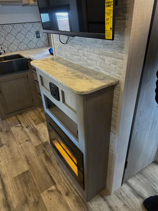RV rental interior showcasing a modern kitchen with sink and an entertainment center featuring a TV and electric fireplace.. Coleman Dutchman Light 2023
