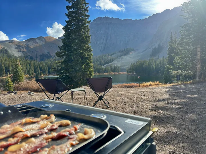 Enjoying a delicious bacon breakfast by the lake with stunning mountain views, perfect for an RV rental outdoor adventure.. Escapod Topo 2 2024