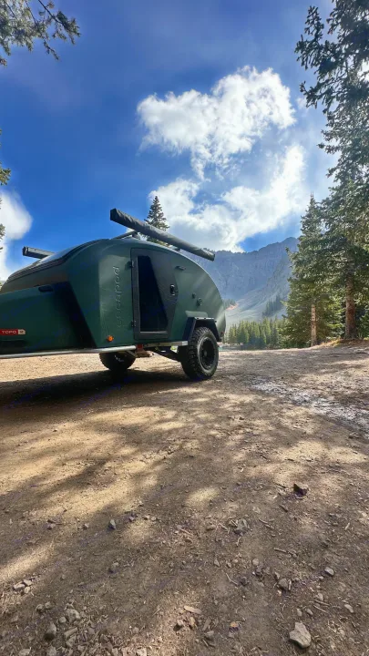 An Escapapod off-road trailer sits on a dirt road near tall pines with mountains behind. Consider this for your next rv rental.. Escapod Topo 2 2024