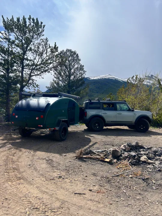 Explore with this RV rental: Grey Ford Bronco towing a green teardrop camper at a mountain campsite.. Escapod Topo 2 2024