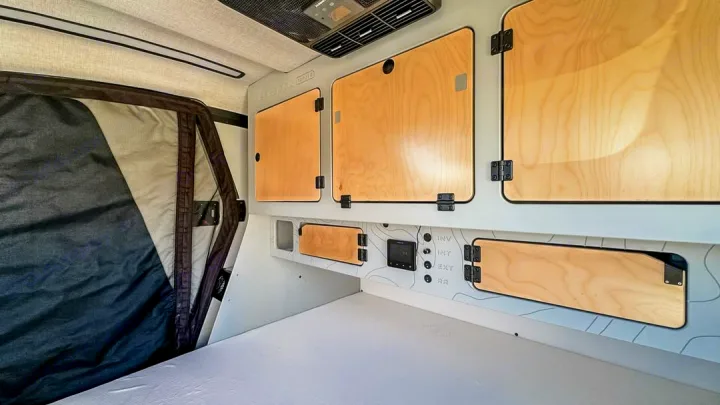 Modern rv rental interior: organized with light wood overhead storage, a system control panel, and a cozy bed area.. Escapod Topo 2 2024