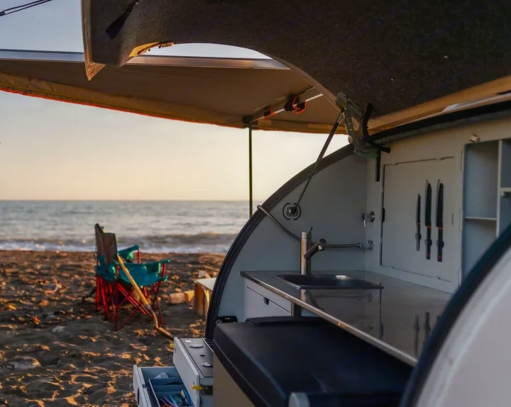 Experience serene beach camping with an RV rental! This setup shows an open teardrop trailer kitchen by the ocean.. Escapod Topo 2 2024