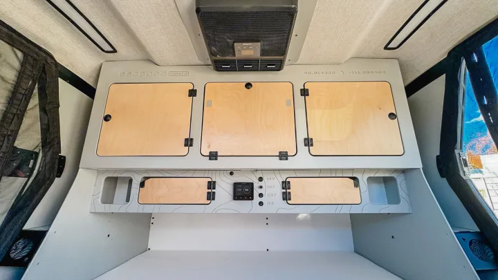 Compact RV rental interior with integrated storage cabinets, intuitive control panel, and overhead AC. Efficient design for travel.. Escapod Topo 2 2024