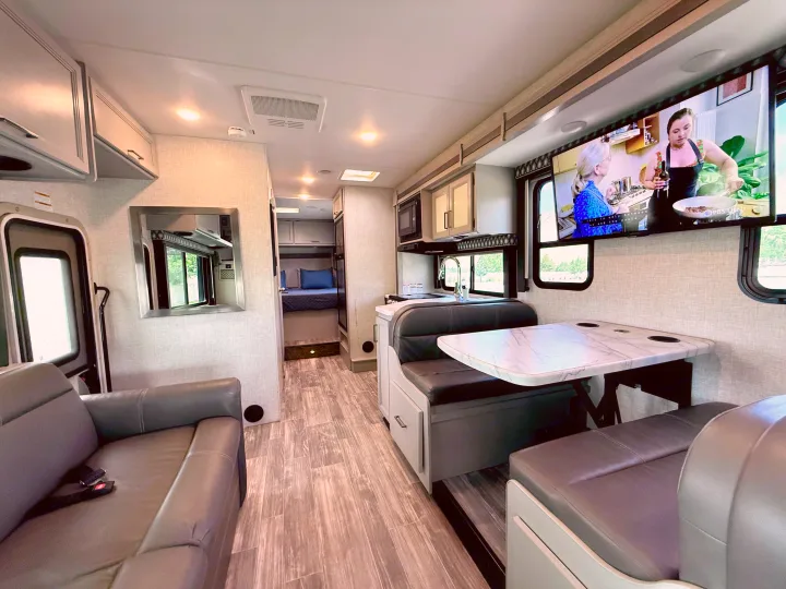 Spacious rv rental interior with modern living area, kitchen, dinette, and a cozy bedroom view.. Thor Geneva 2022