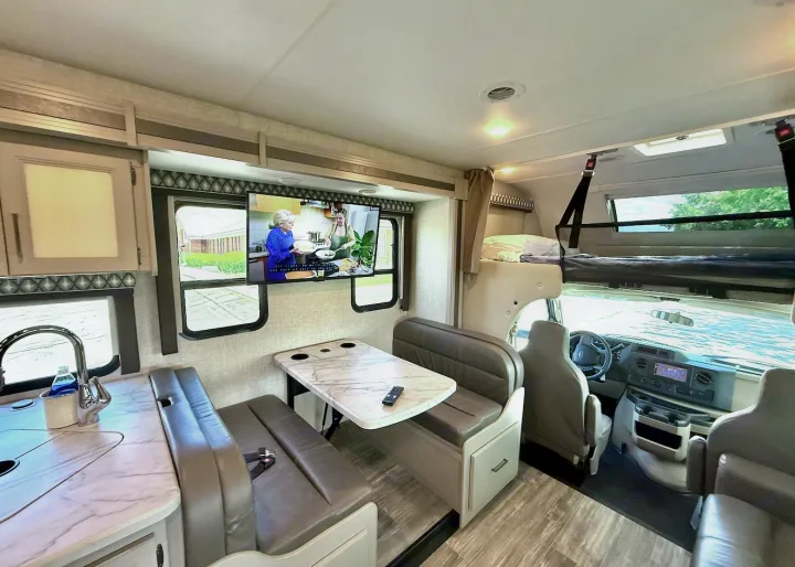 Modern rv rental interior: kitchen, dining, TV, and overhead bunk. Perfect for road trips.. Thor Geneva 2022