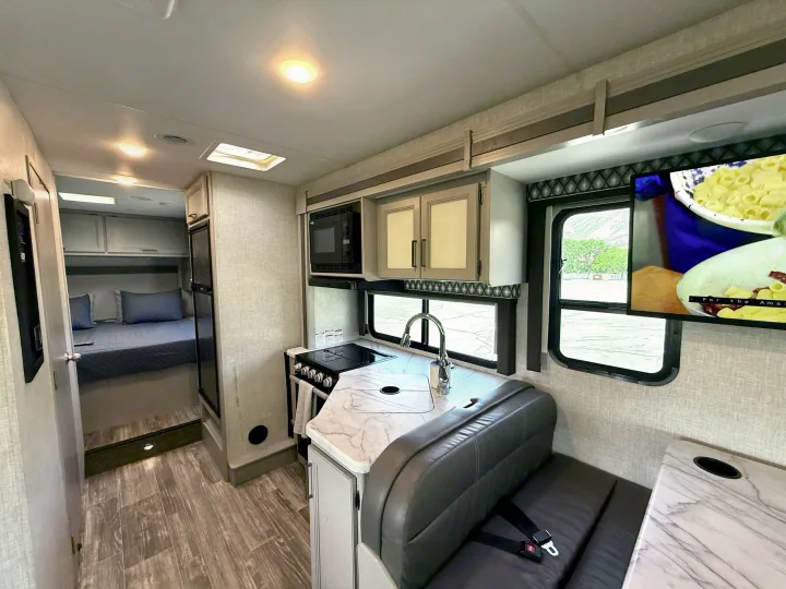 RV rental interior showing a modern kitchen, dining booth, and peek into the comfortable bedroom area.. Thor Geneva 2022