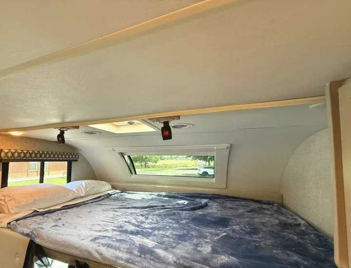Inside a comfortable RV rental: a plush bed, wide windows with outdoor views, and a ceiling skylight.. Thor Geneva 2022