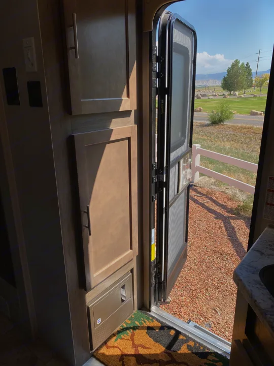 Inside an RV rental, looking out an open screen door to a fenced scenic landscape. Cabinets & electrical panel visible.. R-Pod Hood River Edition 2018