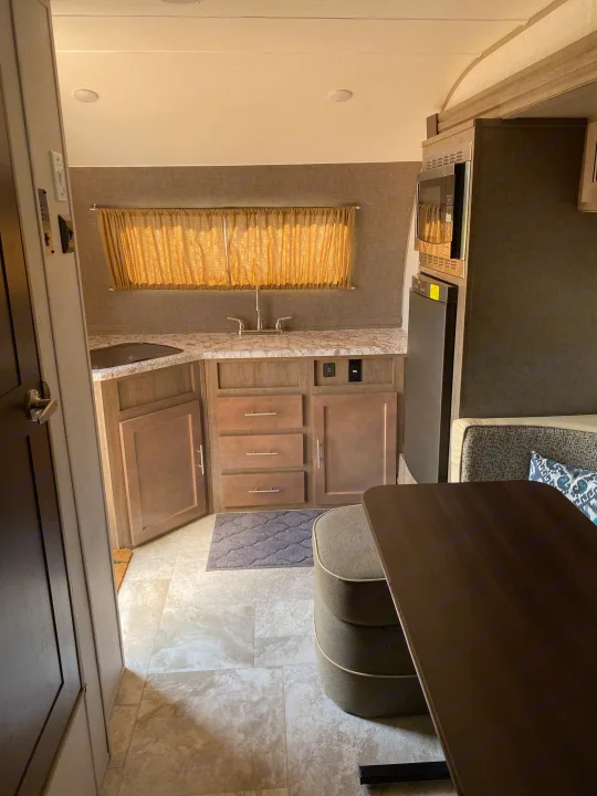Inside an RV rental, a compact living space shows a fully equipped kitchen, adjacent dining area with built-in seating.. R-Pod Hood River Edition 2018