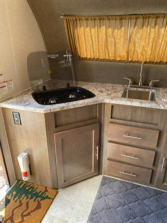 RV rental interior: A compact kitchen area, displaying a stainless steel sink, two-burner stovetop, and wood-look cabinets.. R-Pod Hood River Edition 2018