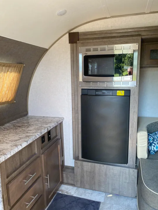 Spacious RV rental interior featuring a modern kitchenette with microwave, refrigerator, and a comfortable dinette area, ideal for travel.. R-Pod Hood River Edition 2018