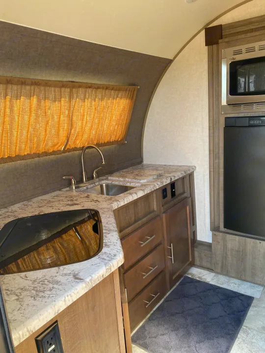 Inside an RV rental, a well-equipped kitchen boasts a sink, microwave, fridge, and cooktop with light filtering curtains.. R-Pod Hood River Edition 2018