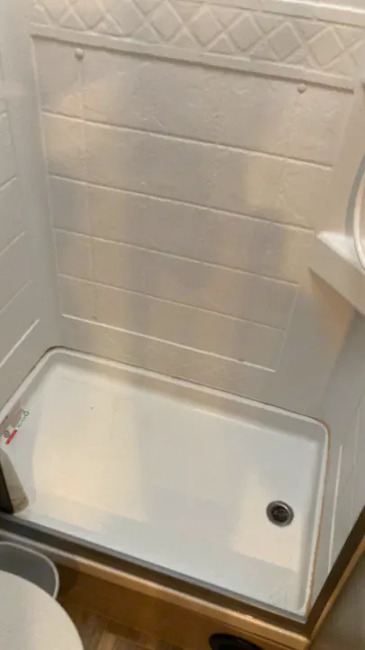 A white, compact shower stall in an RV rental. Features textured walls, a clean shower pan, and a visible drain.. Thor Four Winds 2022