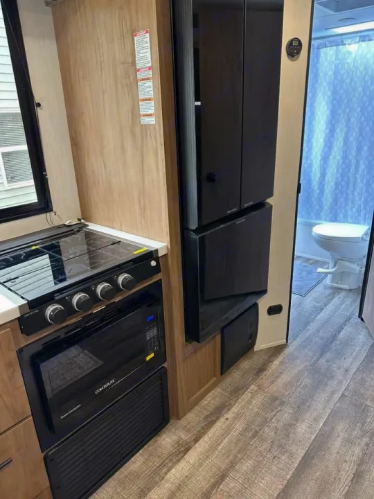 RV rental with a modern kitchen: gas stove, microwave, and refrigerator. Beyond, a compact bathroom. Perfect for travel.. Forest River Campsite Ultra 26CJL 2025