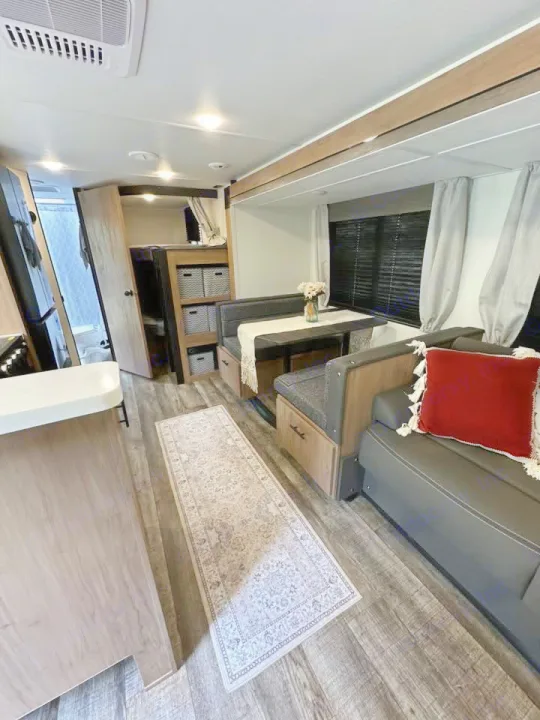Explore this modern RV rental interior featuring a cozy dining nook, lounge sofa, and functional kitchen area.. Forest River Campsite Ultra 26CJL 2025