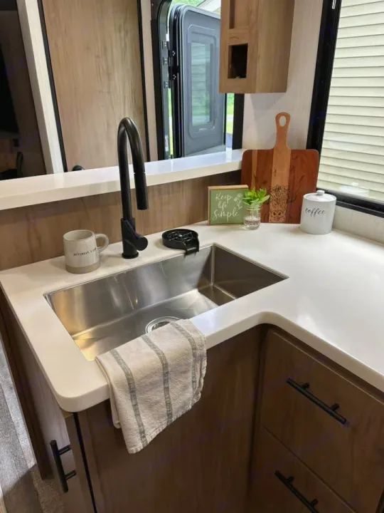 This clean RV rental kitchen features a modern sink, white counters, and charming decor for comfortable mobile living.. Forest River Campsite Ultra 26CJL 2025