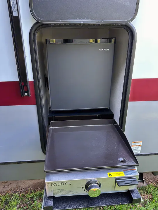 RV rental: Exterior compartment showing a pull-out Greystone griddle and Contoure portable fridge for outdoor meals.. Forest River Campsite Ultra 26CJL 2025