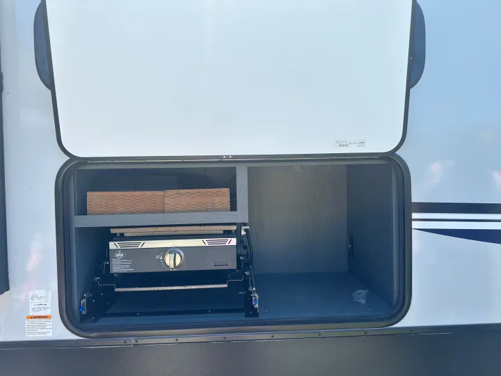 Open RV rental exterior compartment showing a built-in Capital griddle and shelving for outdoor cooking.. Keystone RV Bullet Crossfire 2024