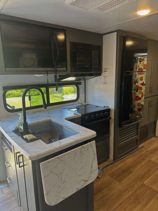 This RV rental features a modern kitchen with marble-look countertops, a sink, stove, microwave, and a mounted TV.. Keystone RV Bullet Crossfire 2024