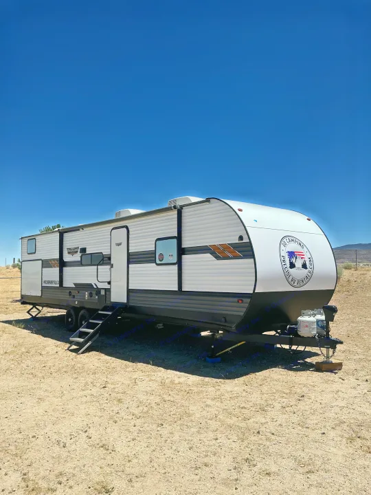 Modern white and gray rv rental parked under a clear blue sky in a dry, open area, ready for adventure.. Forest River Wildwood 2020