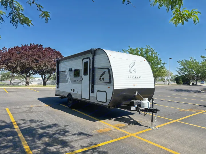 A white and gray 'GO > PLAY' travel trailer, ideal for RV rental, sits in a sunny parking lot under clear skies.. Wayfinder RV Go Play 19BH 2025