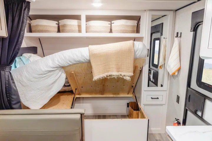 Inside this RV rental, a bed lifts to reveal hidden storage. Overhead shelves, a mirror, and amenities optimize compact living.. Wayfinder RV Go Play 19BH 2025