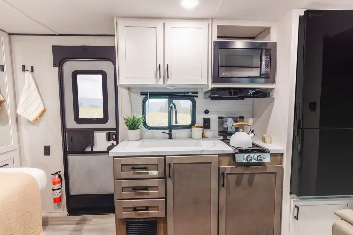 Modern RV rental kitchen area features a sink, microwave, stove, and black fridge. Compact and ready for adventure.. Wayfinder RV Go Play 19BH 2025