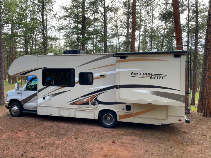A spacious Class C rv rental, a Freedom Elite motorhome, with its slide-out extended, parked in a pine forest campsite.. Thor Freedom Elite 2017