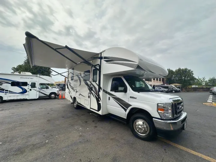 Experience freedom with an RV rental. Two white Class C motorhomes, one with an extended awning, are parked in a lot.. Jayco Redhawk 2021
