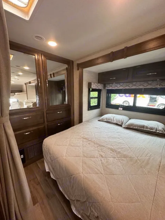 RV rental: Bright bedroom with queen bed, dark wood storage, mirrored wardrobe, and natural light from skylight.. Jayco Redhawk 2021