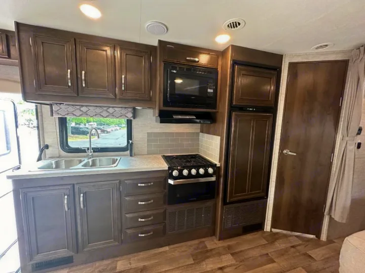 RV rental kitchen. Dark wood cabinets, double sink, stove, microwave, and fridge provide home comfort on the road.. Jayco Redhawk 2021