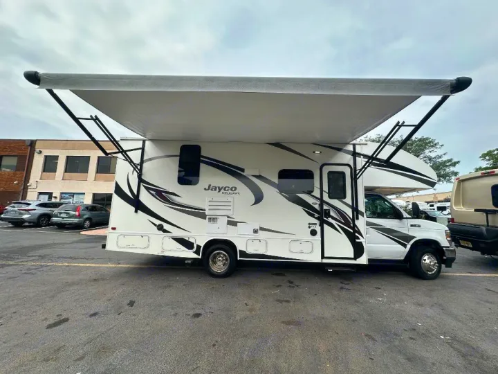 White Jayco Redhawk RV rental with a large, extended grey awning, parked in a lot. Ready for your next adventure.. Jayco Redhawk 2021