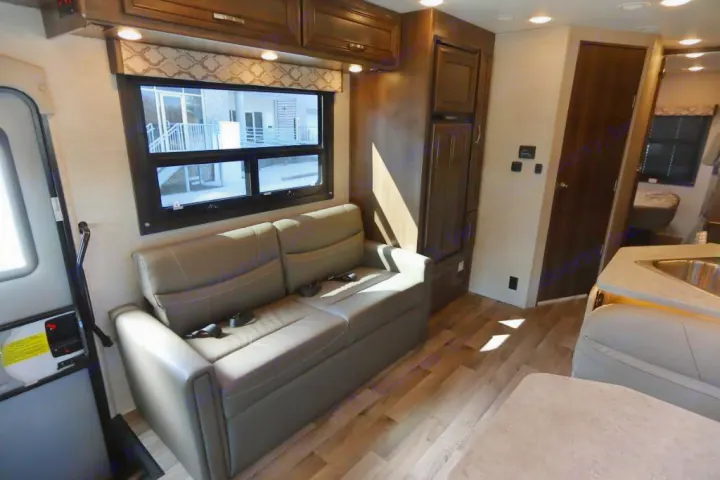Spacious rv rental living area features a comfy sofa, large window, kitchen, and modern wood flooring.. Jayco Redhawk 2021