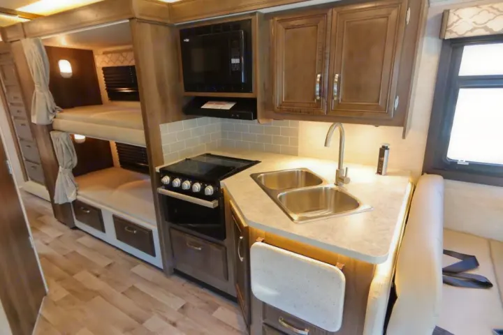 Explore this RV rental's cozy interior, featuring a functional kitchen, bunk beds, and comfortable dinette seating.. Jayco Redhawk 2021