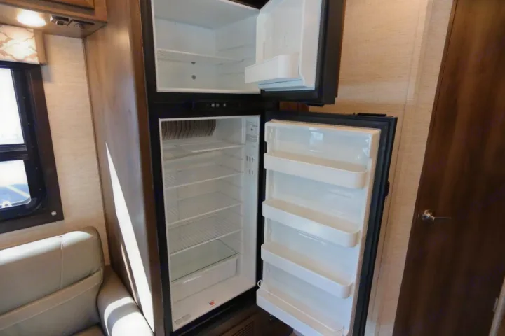 Empty two-door refrigerator in an RV rental, open to show clean shelves in both fridge and freezer compartments.. Jayco Redhawk 2021