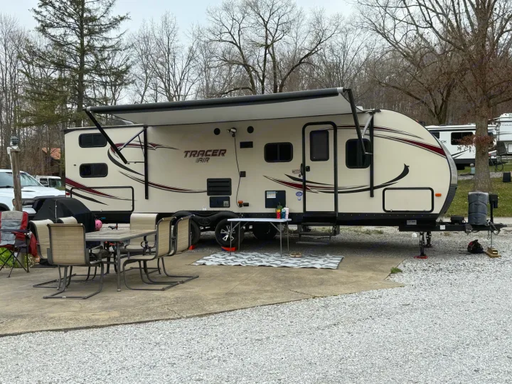 Spacious Tracer Air travel trailer RV rental set up at a gravel campsite with an extended awning, outdoor dining area, and patio mat.. Forest River Tracer Air 2016