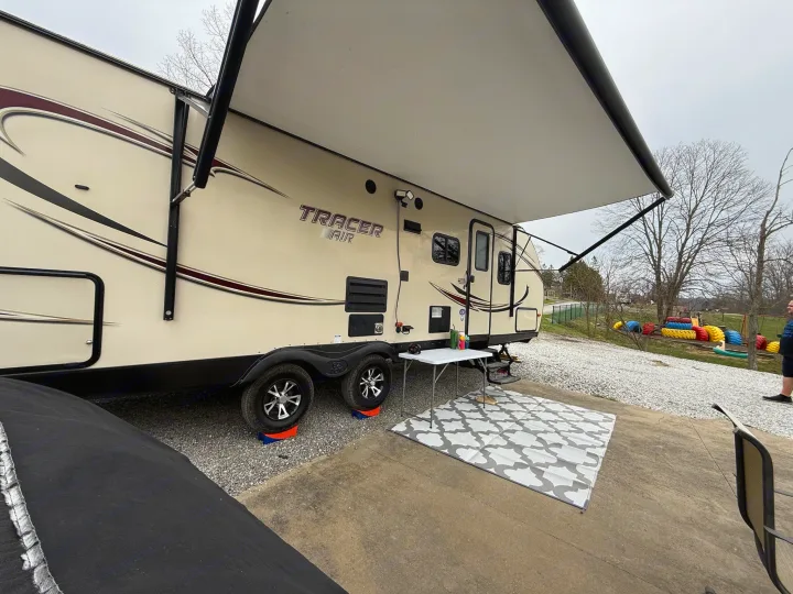 A beige RV with its awning extended creates a comfortable outdoor space, ideal for an RV rental adventure.. Forest River Tracer Air 2016