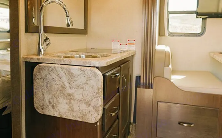Compact RV rental interior featuring a kitchenette with sink, counter extension, and a bright dinette area.. Thor Chateau Sprinter 2020