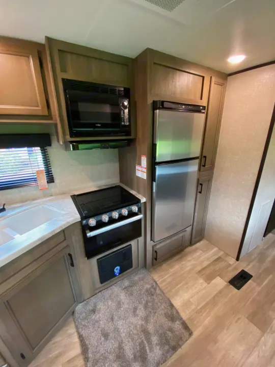 Step inside this RV rental's well-equipped kitchen, featuring a microwave, stove, sink, and refrigerator.. Jayco Jay Flight SLX 2022