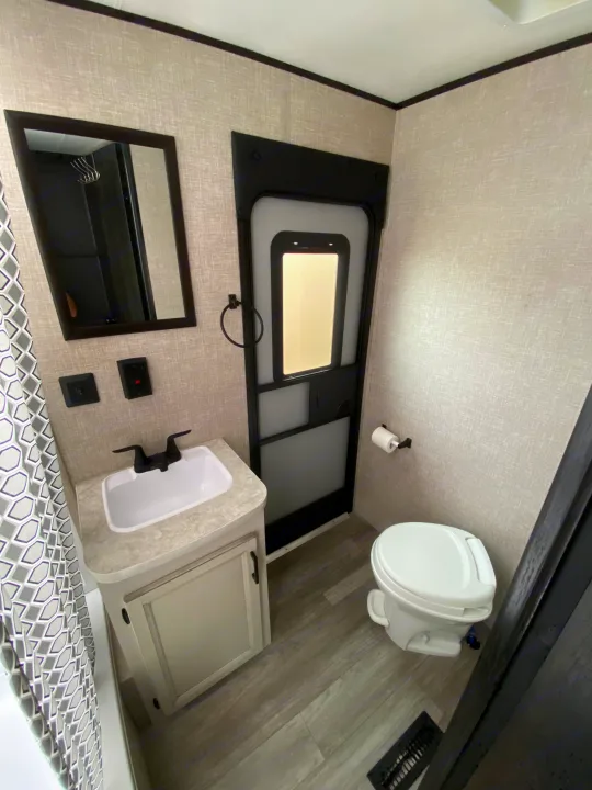 This RV rental's compact bathroom features a white toilet, vanity with sink, mirror, and a patterned shower curtain.. Jayco Jay Flight SLX 2022