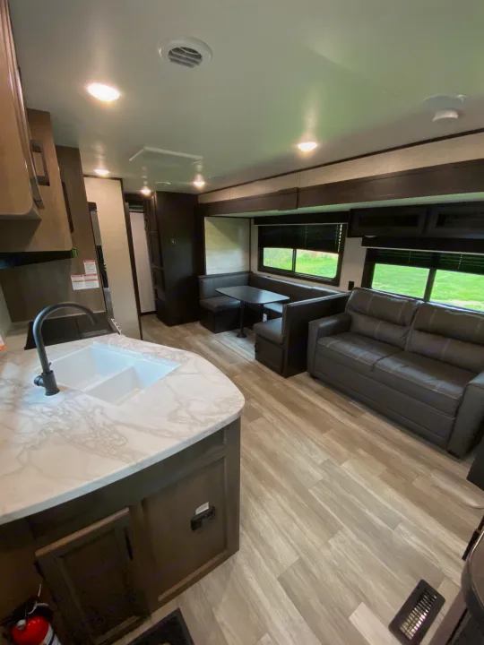 Spacious RV rental interior: kitchen with sink, dining booth, and cozy sofa on light wood-look flooring.. Jayco Jay Flight SLX 2022